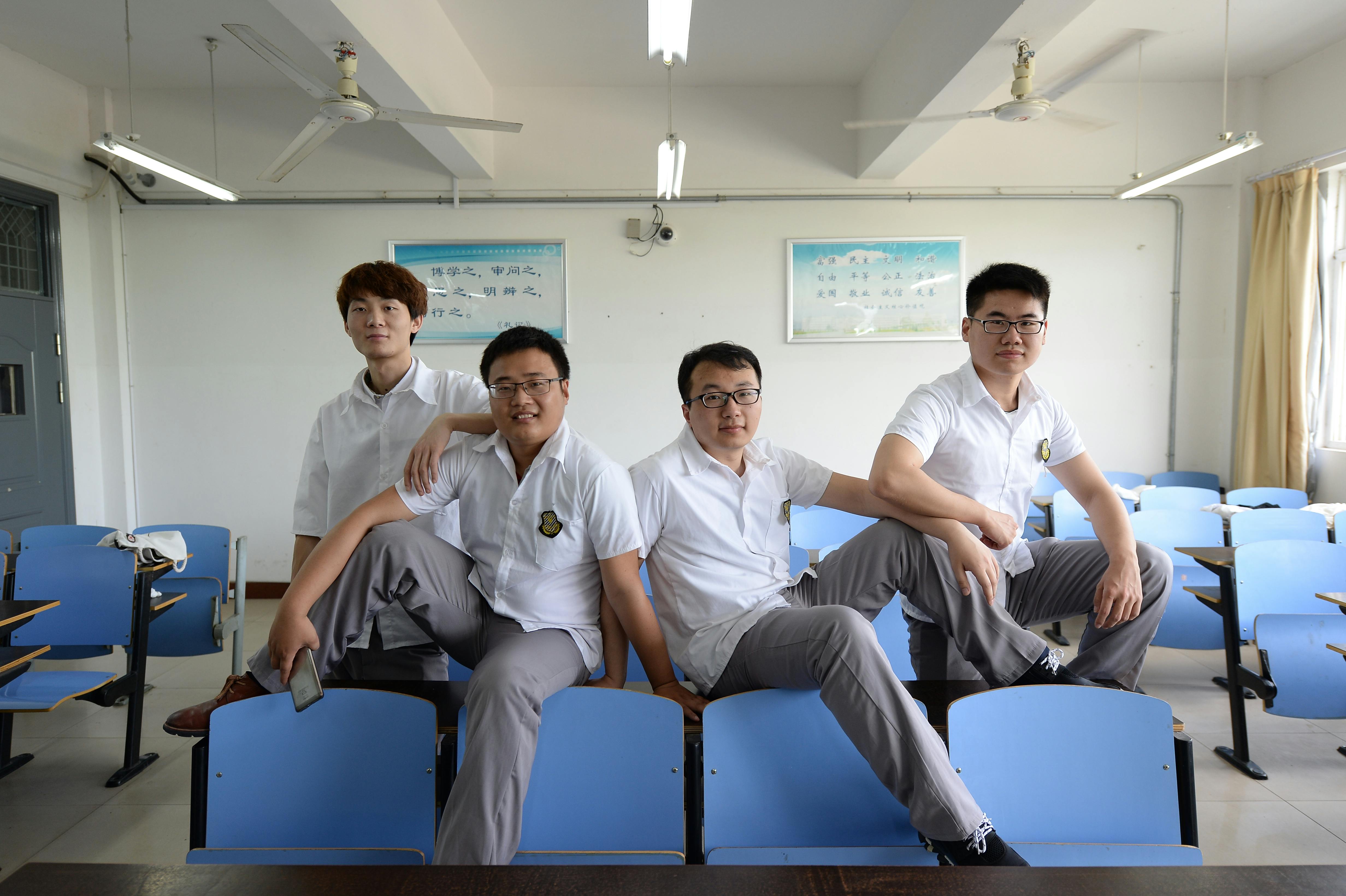 Four students posing confidently in a classroom with blue chairs, showcasing friendship and teamwork.