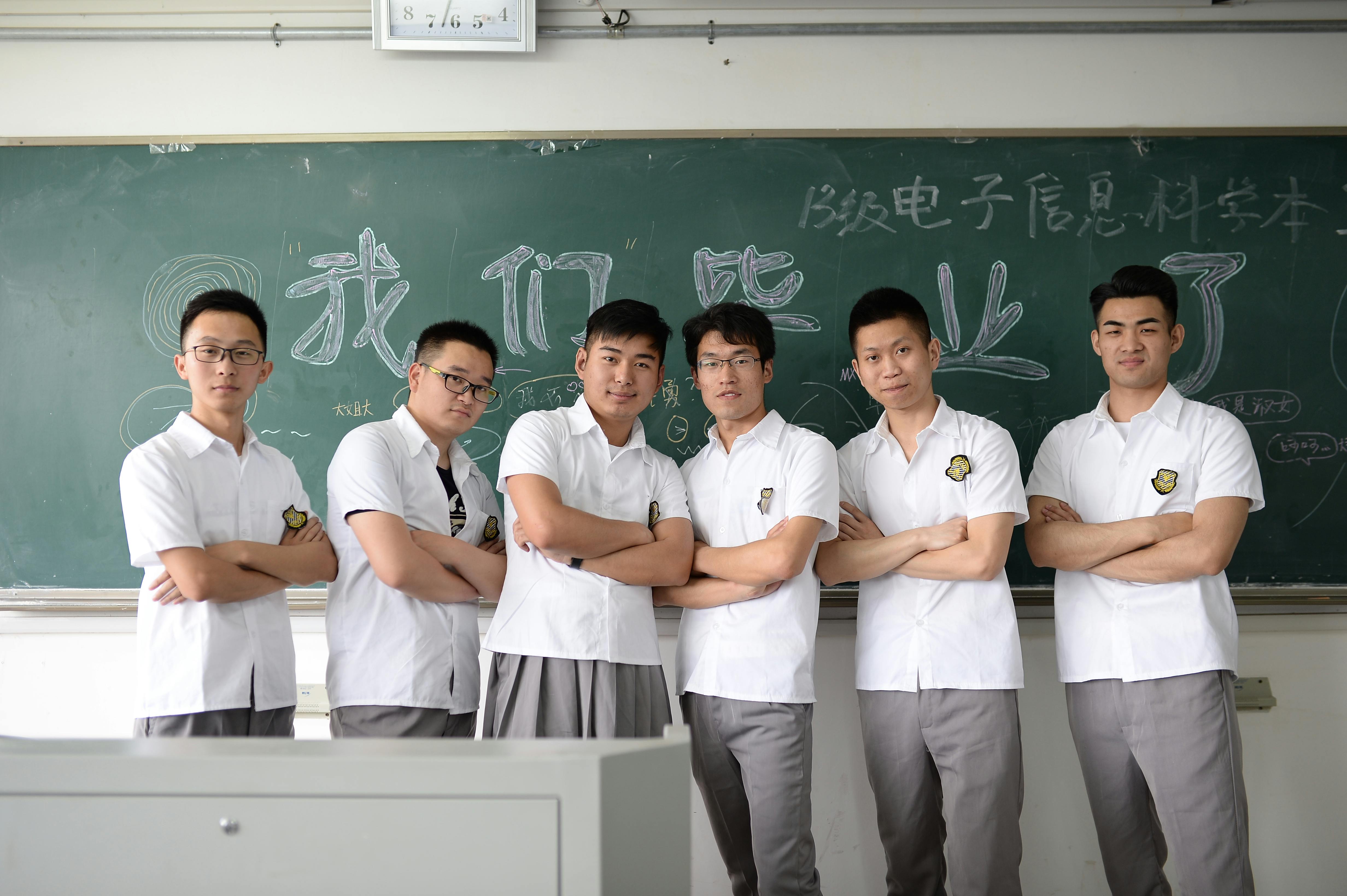 Group of male students standing confidently in classroom setting with chalkboard background.