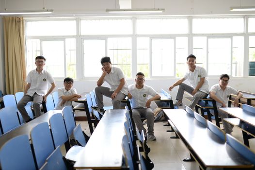 Young students in uniform sitting in a bright classroom, posing casually.