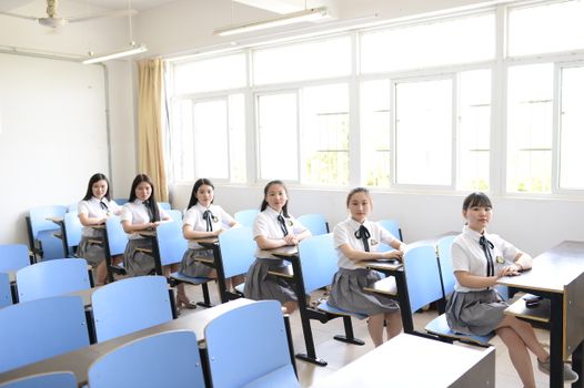 Group of Asian female students sitting in a well-lit classroom, ready for a lecture.