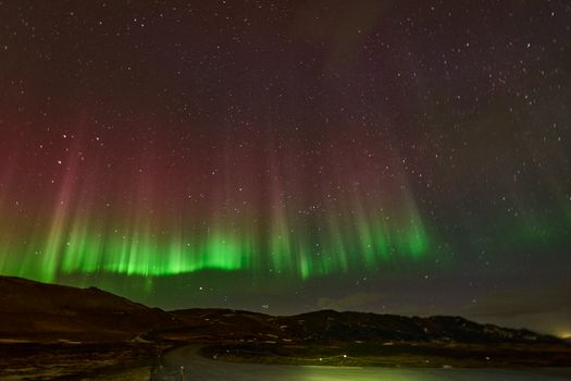 Vivid aurora borealis dancing over Þingeyjarsveit, Iceland's dark sky.