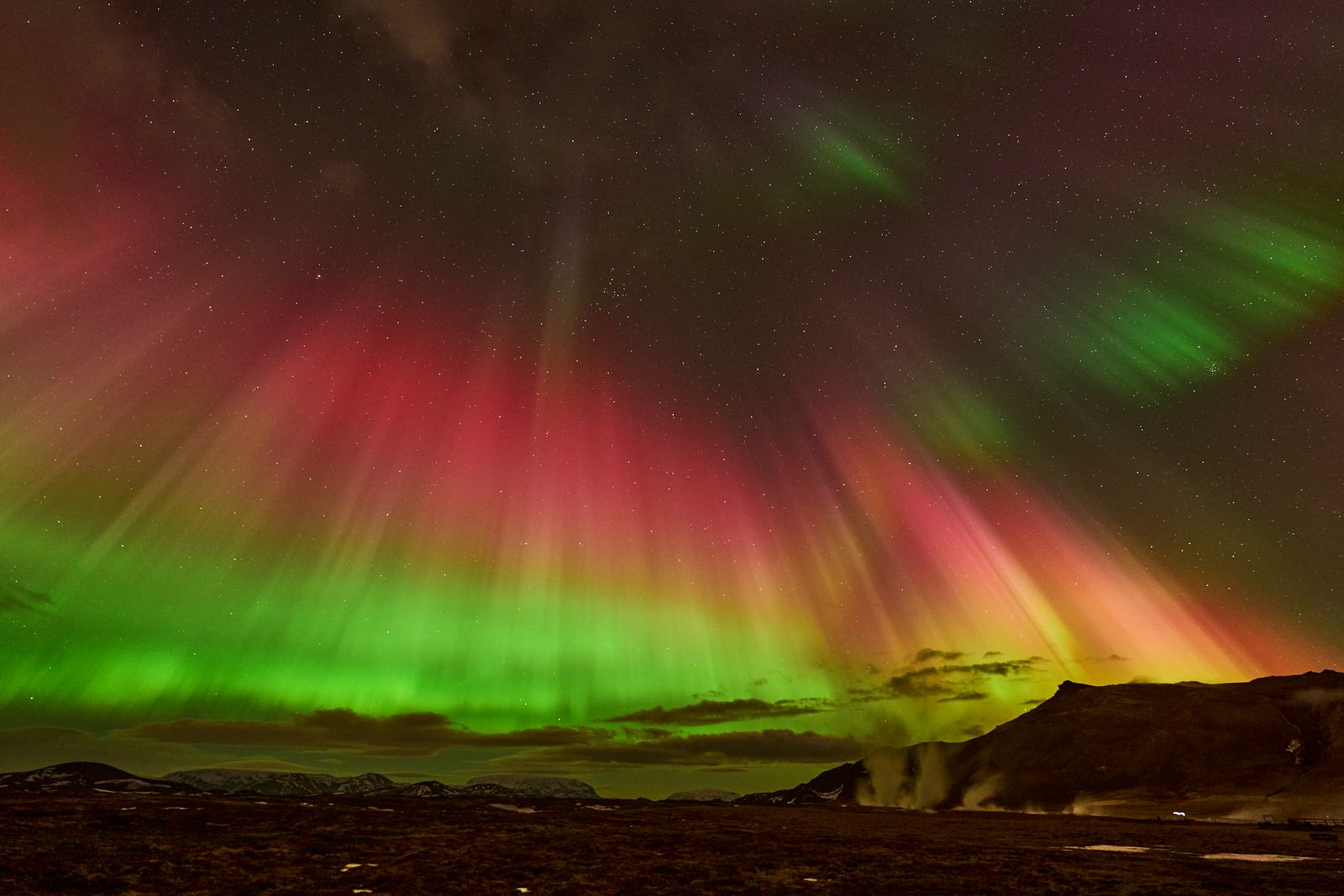Green and red Northern Lights glowing over a dark Icelandic landscape