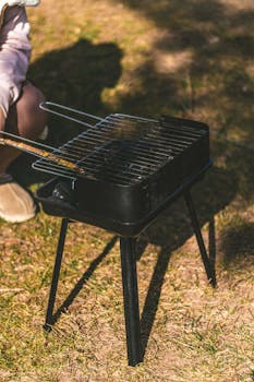 Compact black grill set on grass outdoors, perfect for portable cooking.