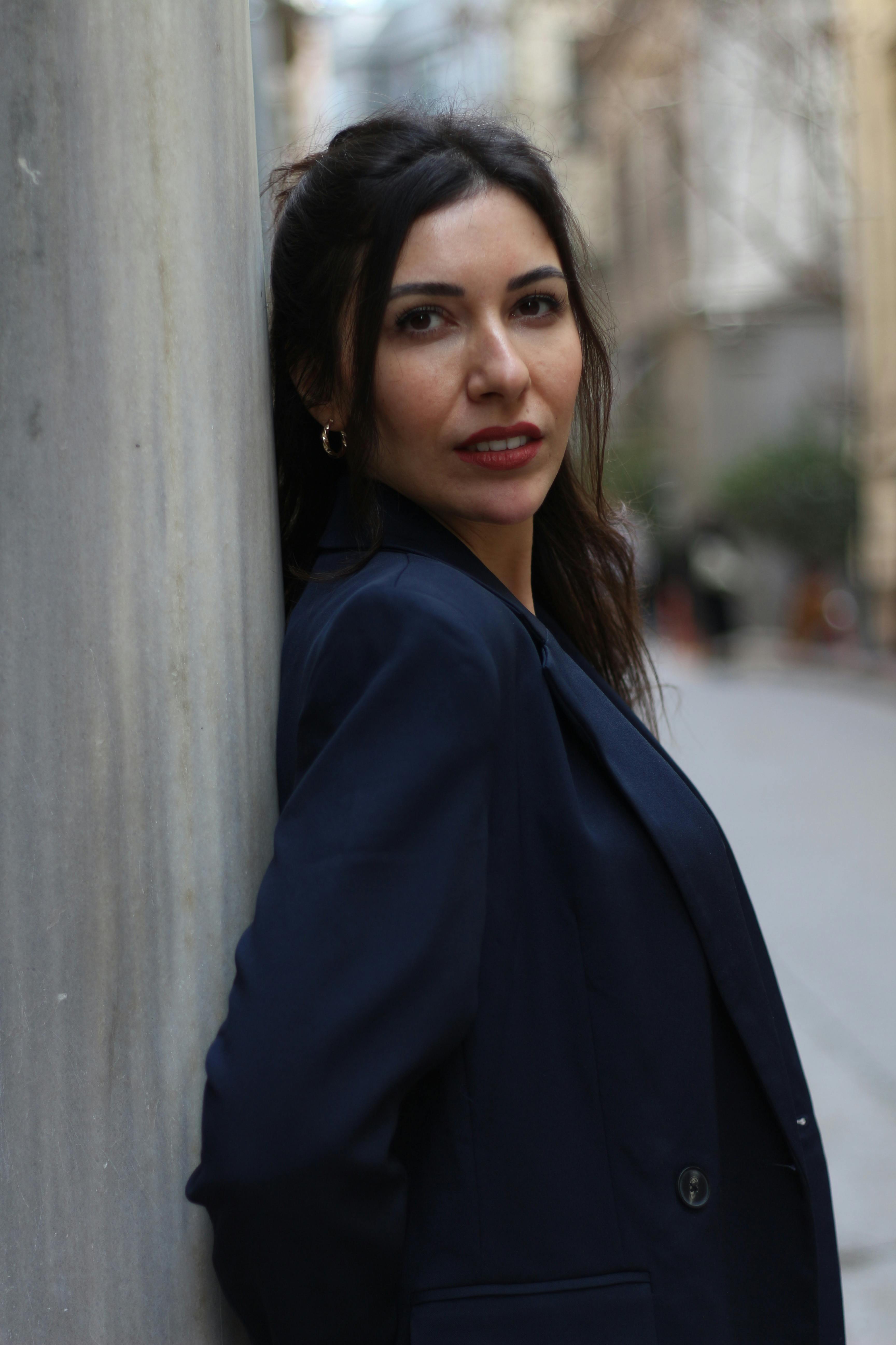 Stylish woman in blue coat leaning against a pillar on an İstanbul street.