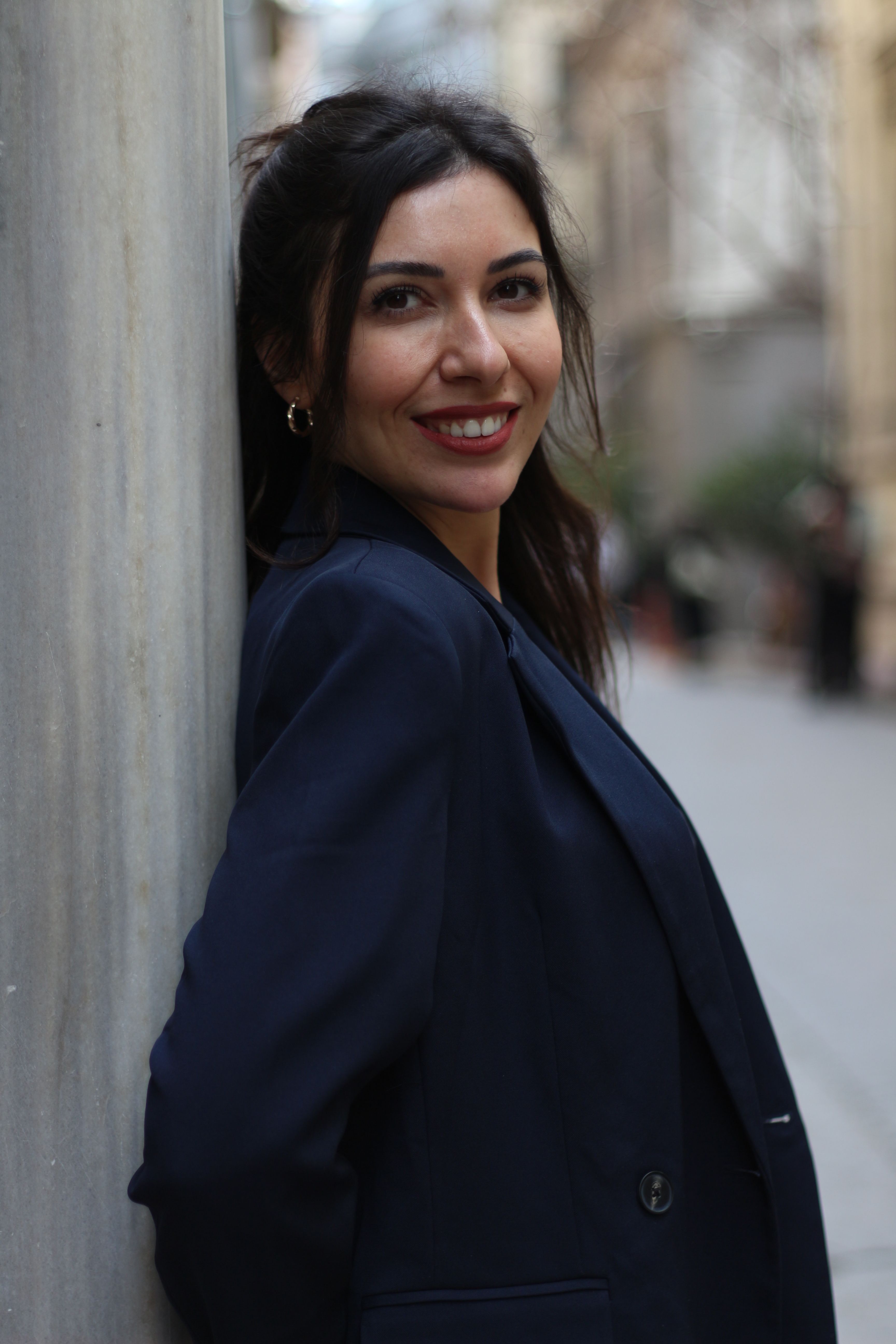 Portrait of a woman smiling against a column in an outdoor İstanbul setting.