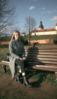 A woman enjoys a sunny day on a bench with Niasvizh Castle in the background.