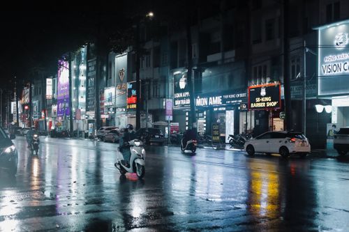 Free Urban street at night with city lights reflecting on wet pavement and moving traffic. Stock Photo