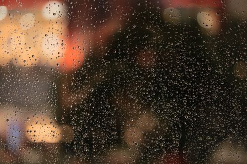 Free Raindrops on window pane with blurred city lights in the background, creating a moody atmosphere. Stock Photo