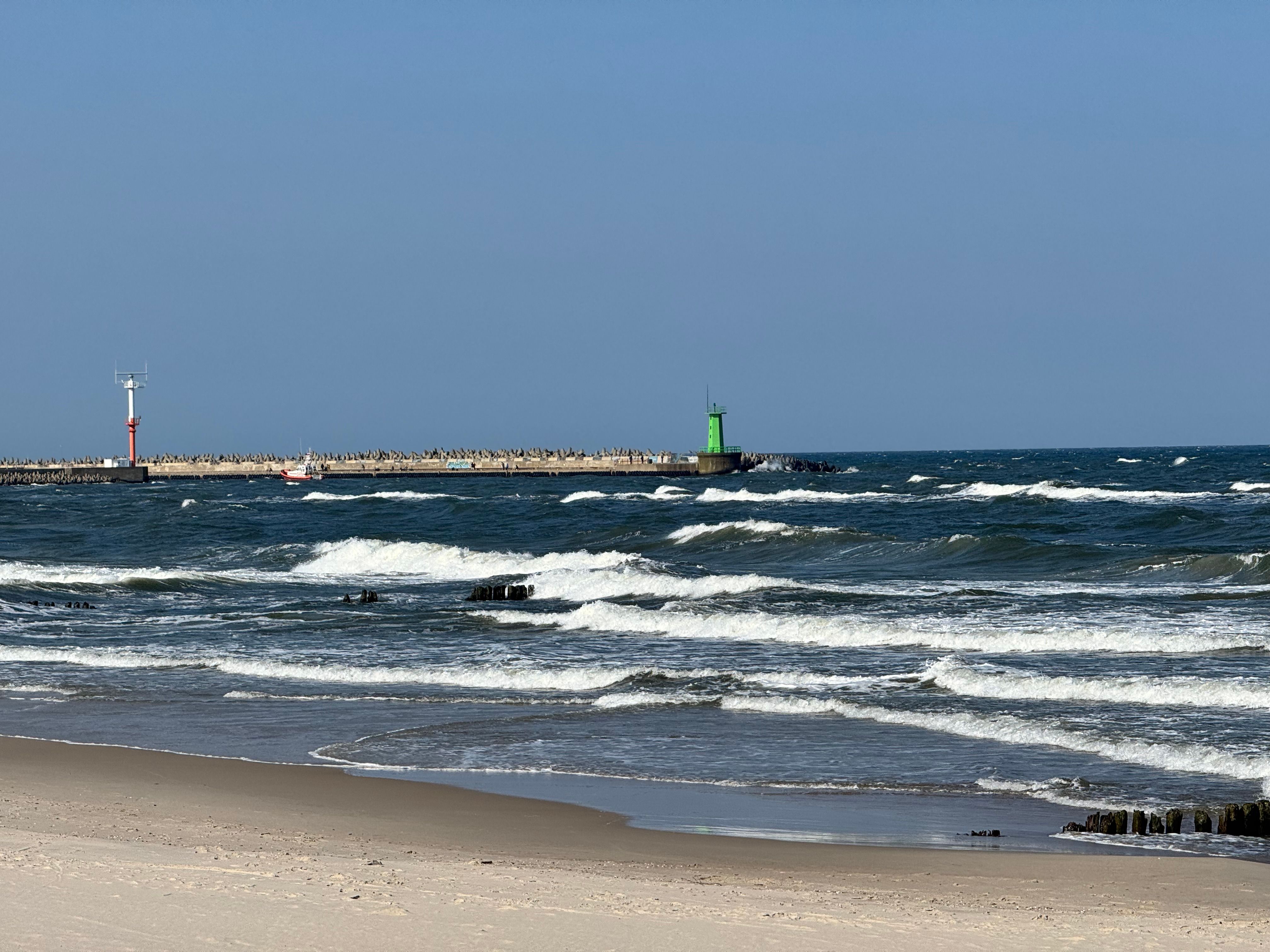 Waves crashing on the sandy shore with distant lighthouses under a clear blue sky.