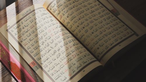 Free An open Quran with Arabic script illuminated by natural sunlight on a wooden surface. Stock Photo