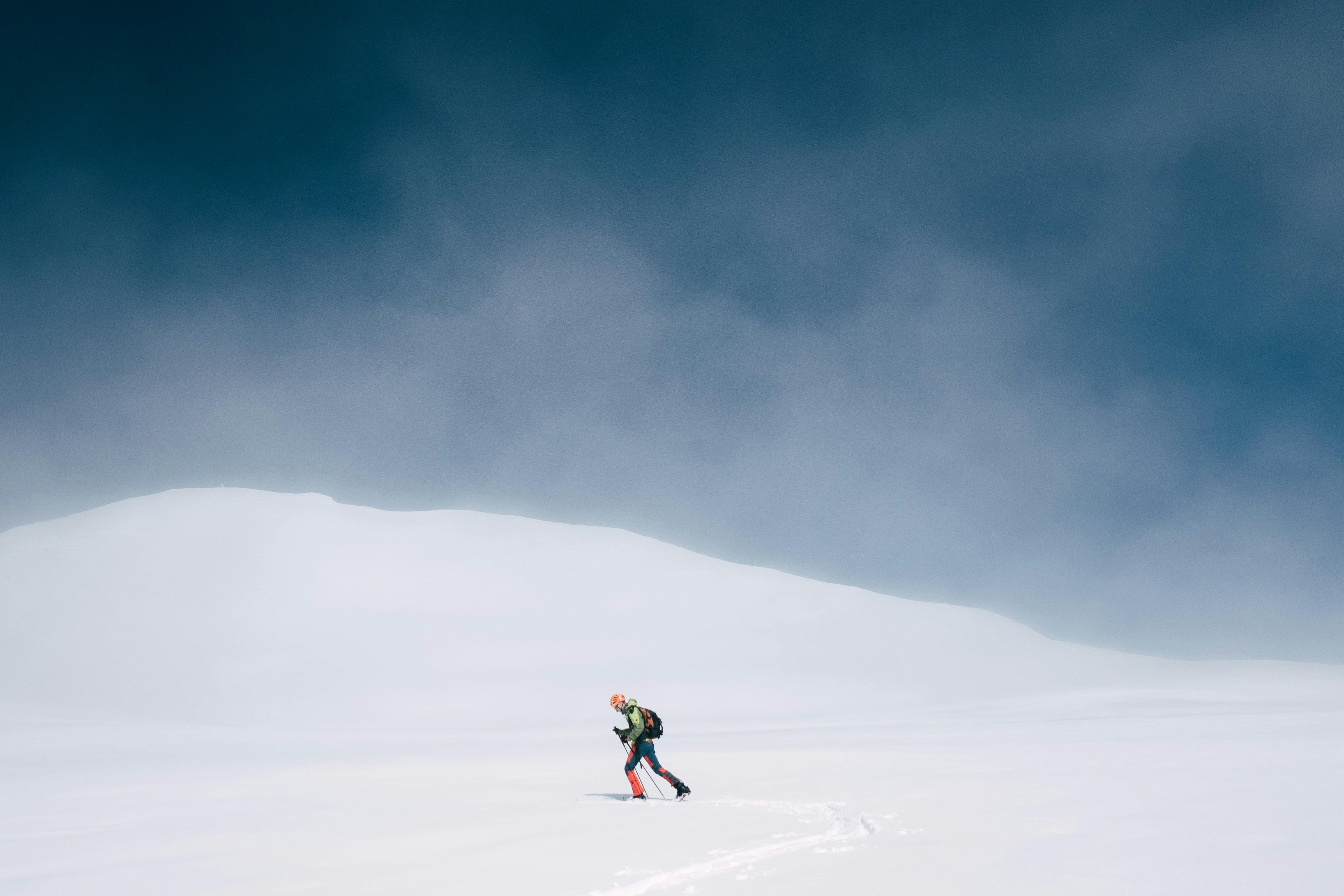 A lone skier traverses a vast, snowy landscape under a clear sky.
