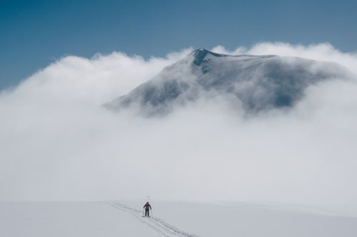 Free A skier glides on a snowy mountain with clouds surrounding a distant peak. Stock Photo