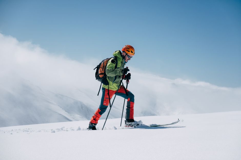 Ski mountaineer exploring snowy mountains under clear blue skies. Adventure and winter sports.