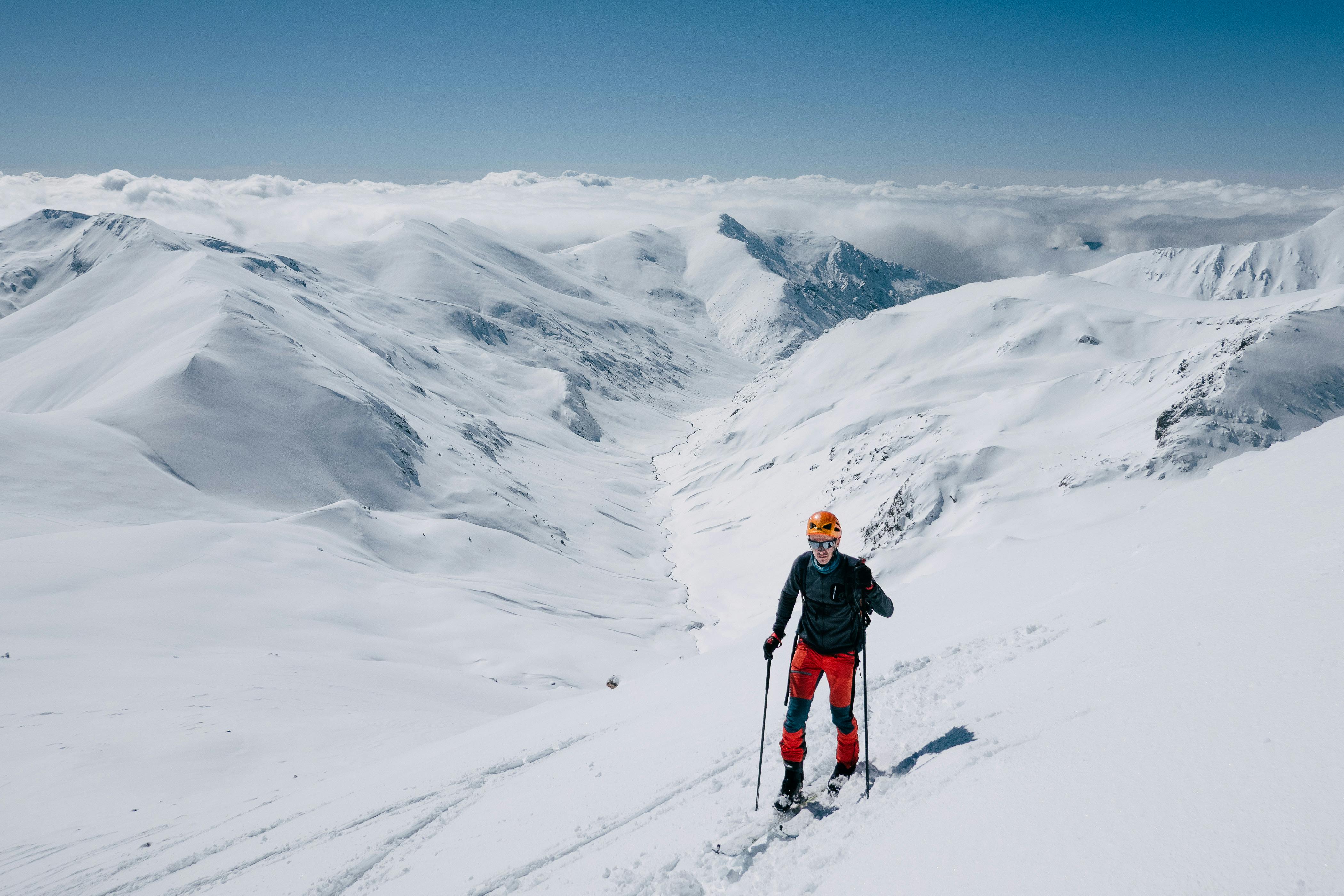 Skier traverses snowy mountains under clear blue skies.