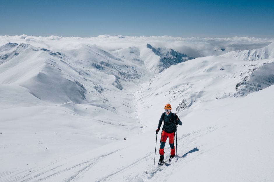Skier traverses snowy mountains under clear blue skies.
