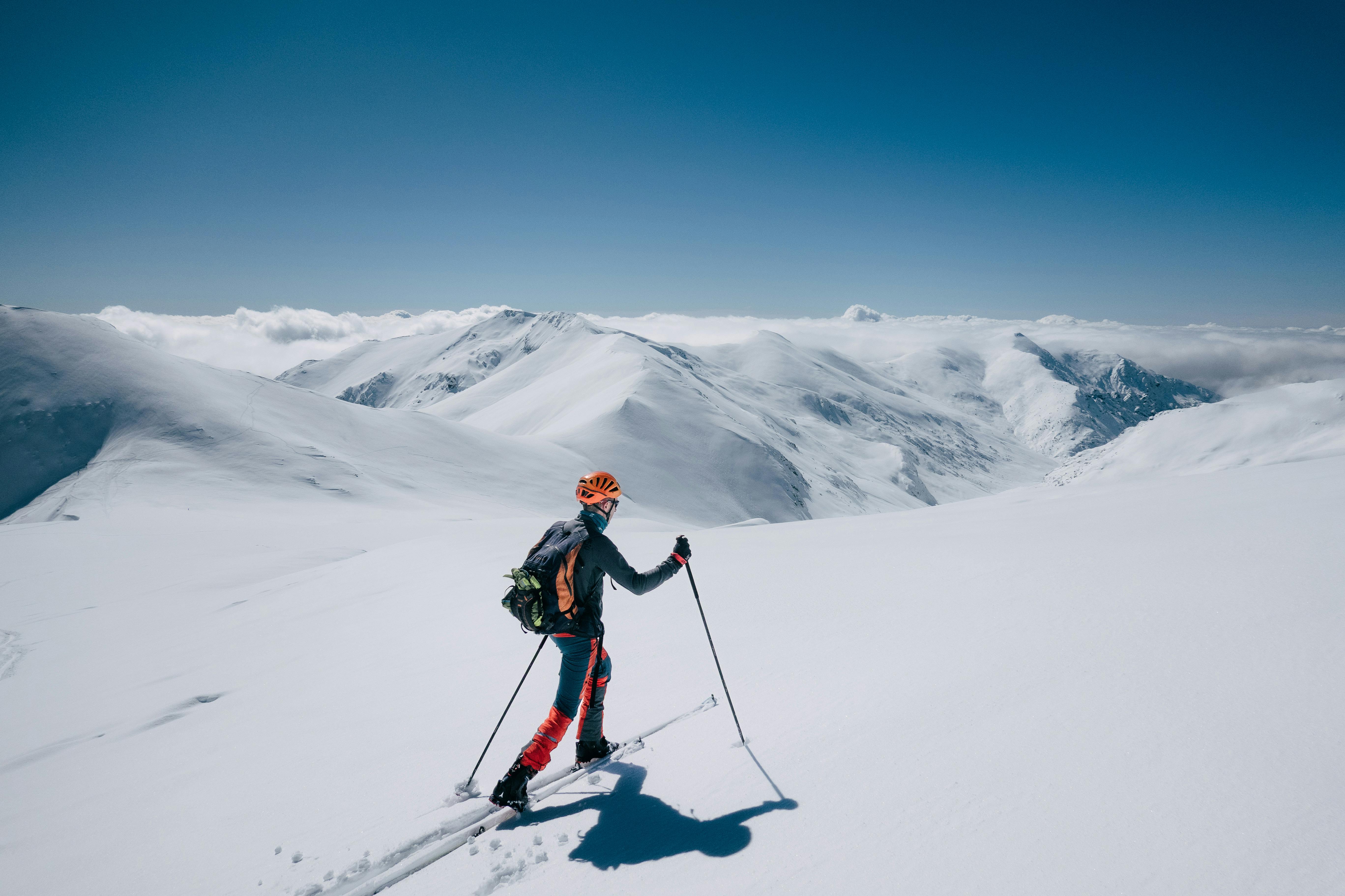 Skier traversing a snowy mountain range on a sunny day.