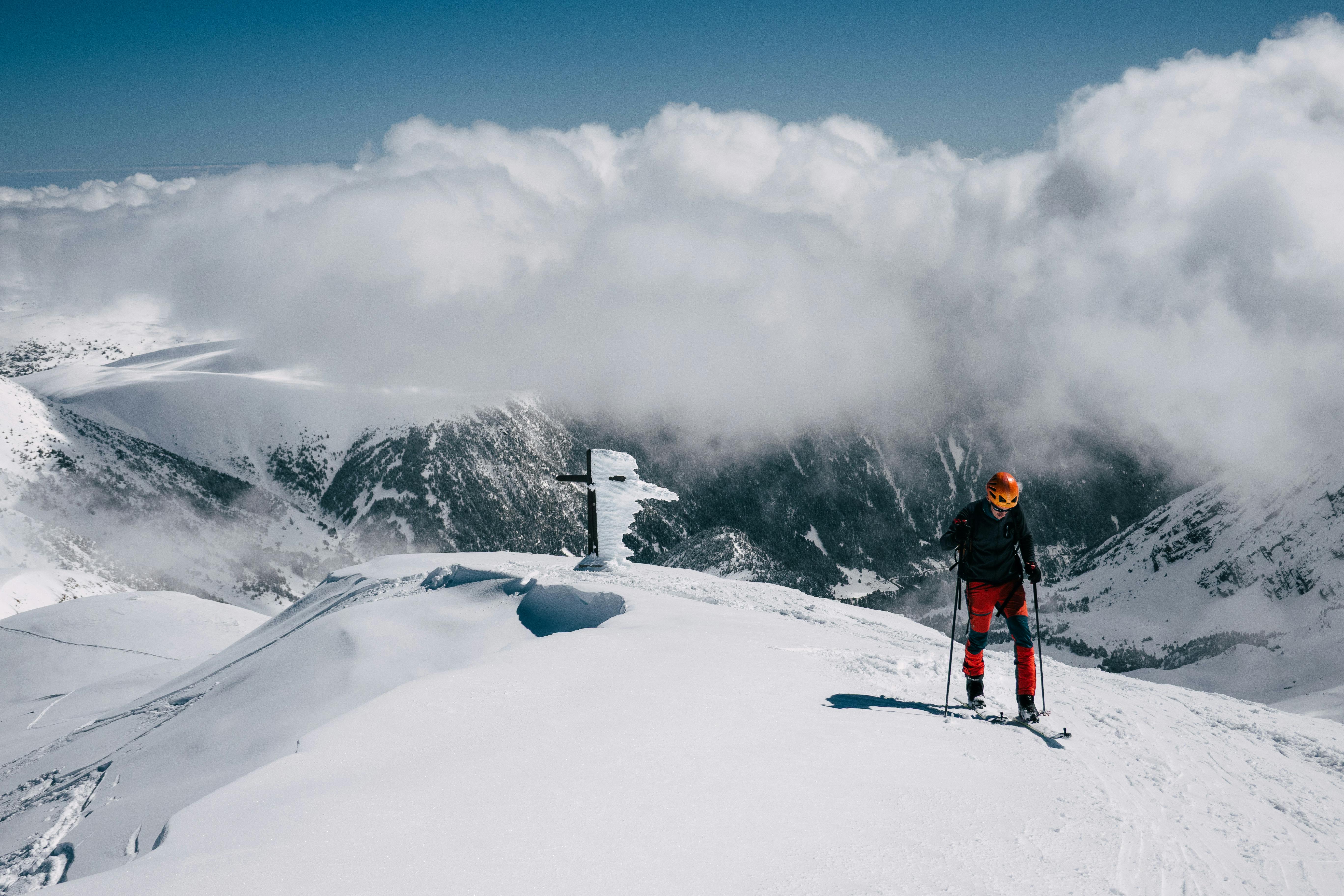 Skier on a snowy mountain peak beneath a sky of clouds, surrounded by stunning scenery.