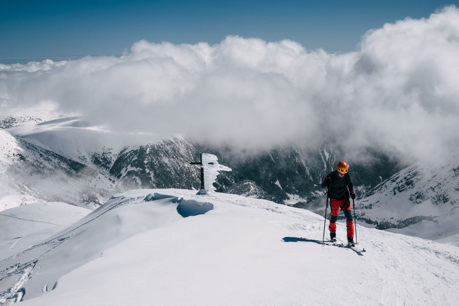 Skier on a snowy mountain peak beneath a sky of clouds, surrounded by stunning scenery.