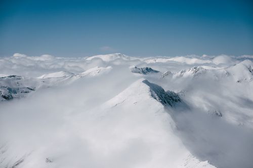 Free Breathtaking aerial view of snow-capped mountains with cloud cover under a clear blue sky. Stock Photo