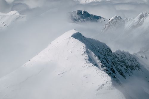 Free A breathtaking aerial shot of snow-covered mountain peaks shrouded in clouds. Stock Photo
