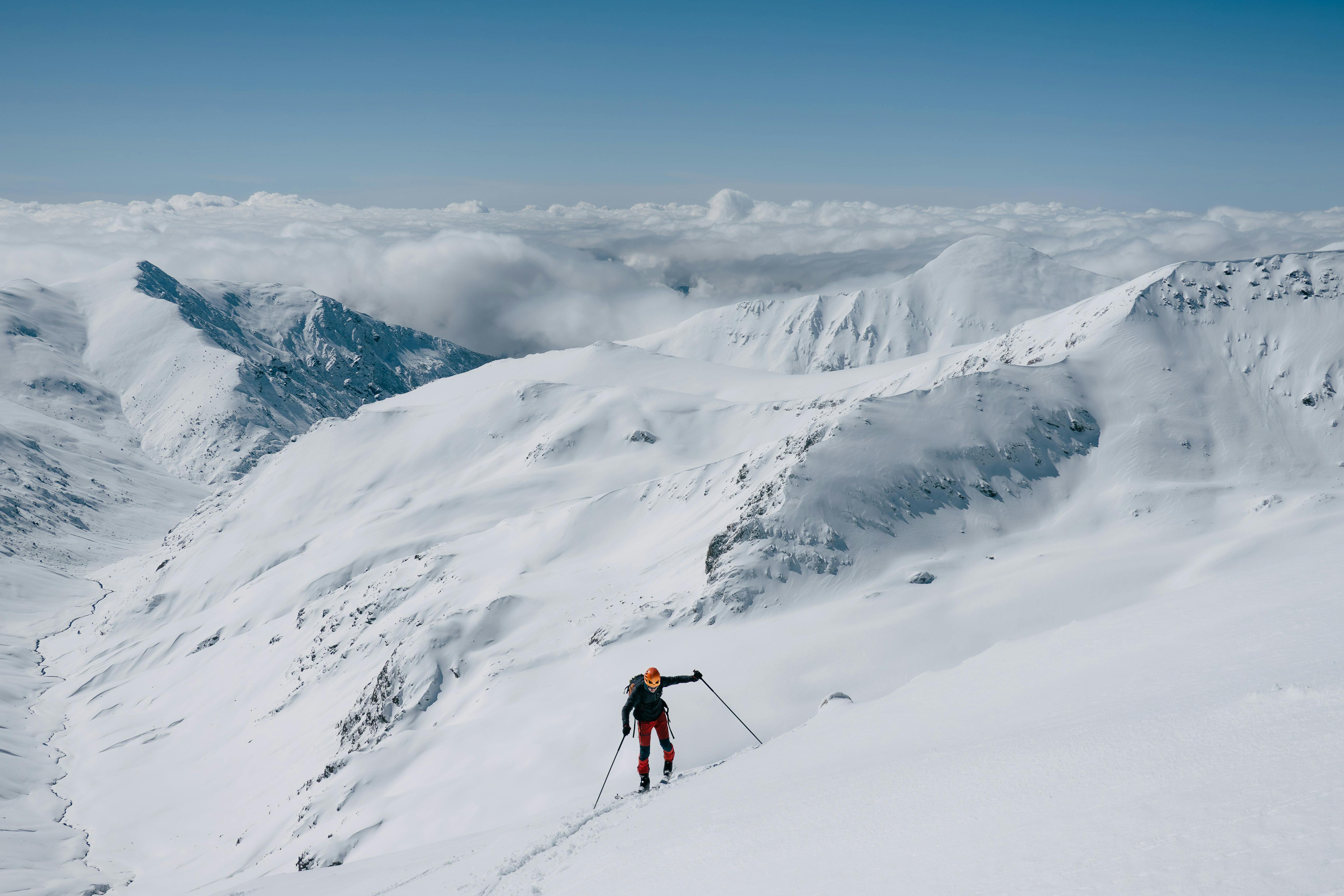 Skier climbing a snowy mountain under clear skies, showcasing winter adventure.