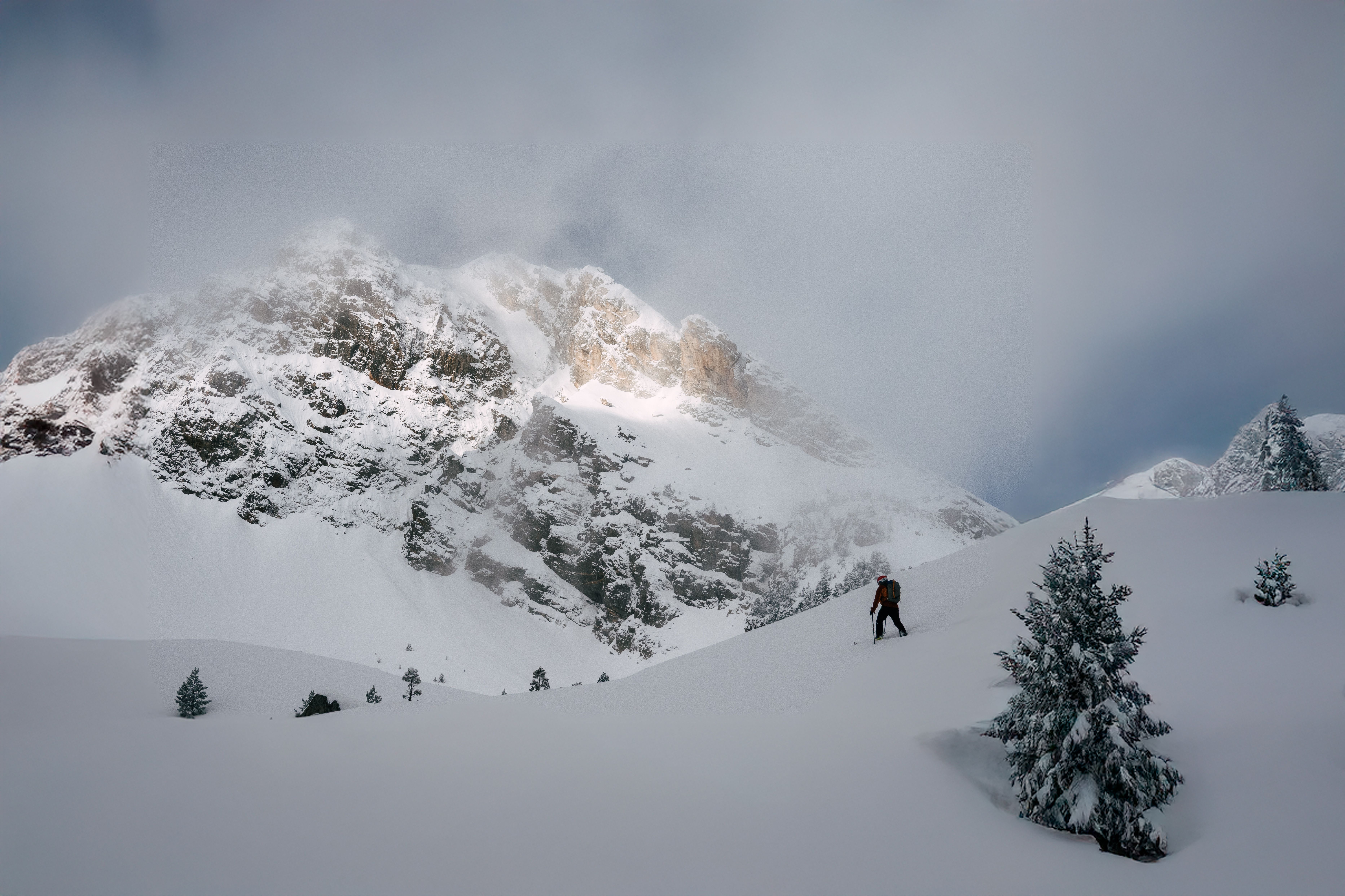A solitary skier traverses a snow-covered mountain slope under a cloudy sky, showcasing winter adventure.