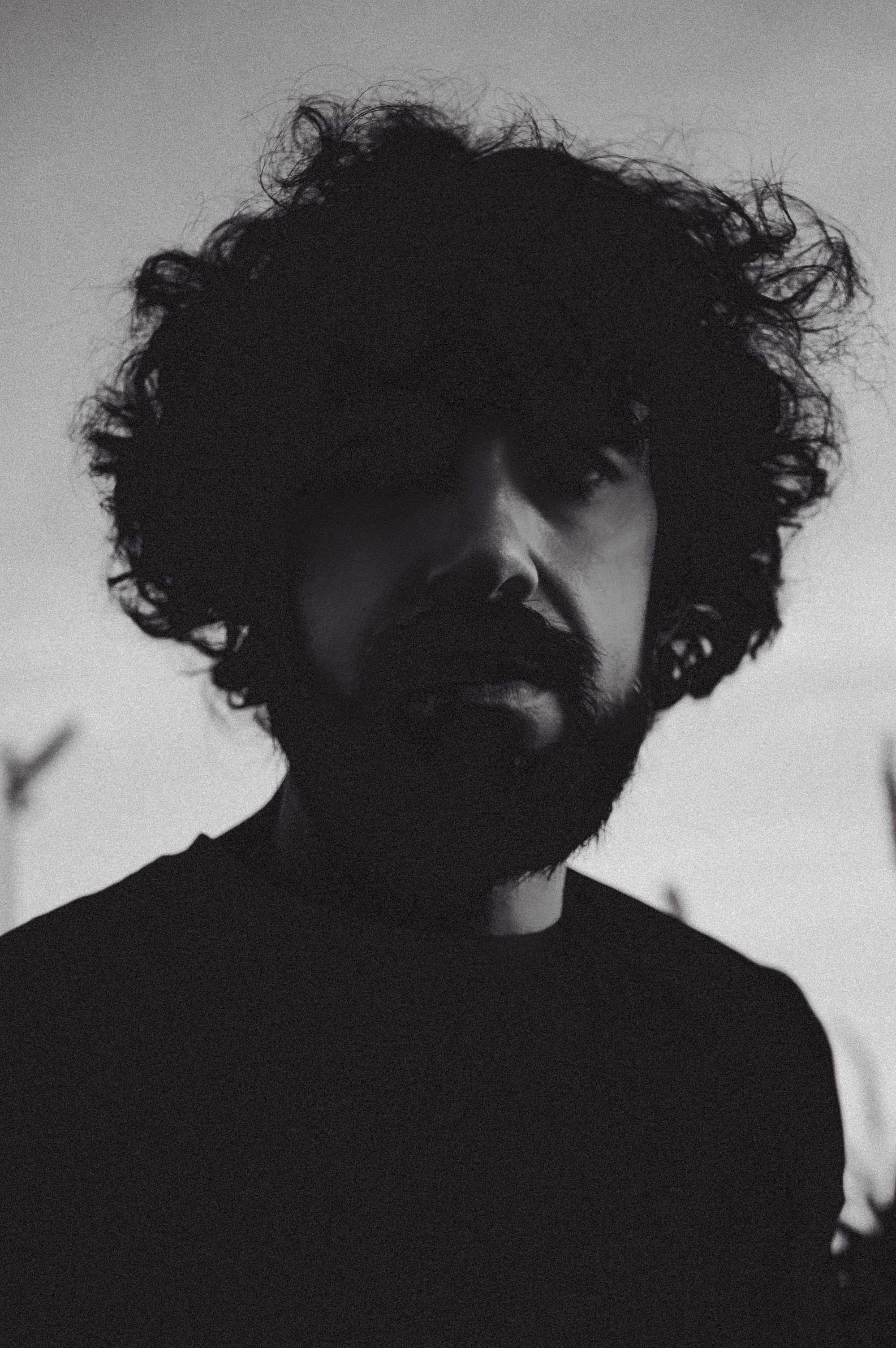 A moody black and white portrait captures a man with curly hair and a beard against a soft background.