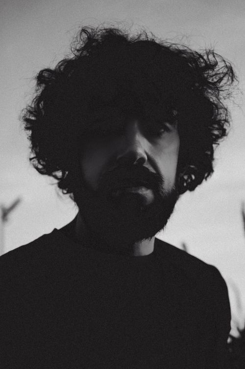 Free A moody black and white portrait captures a man with curly hair and a beard against a soft background. Stock Photo