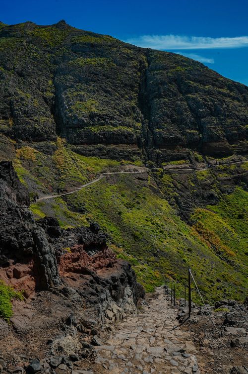 Free A scenic pathway winding through a rocky mountain with lush greenery under a clear blue sky. Stock Photo