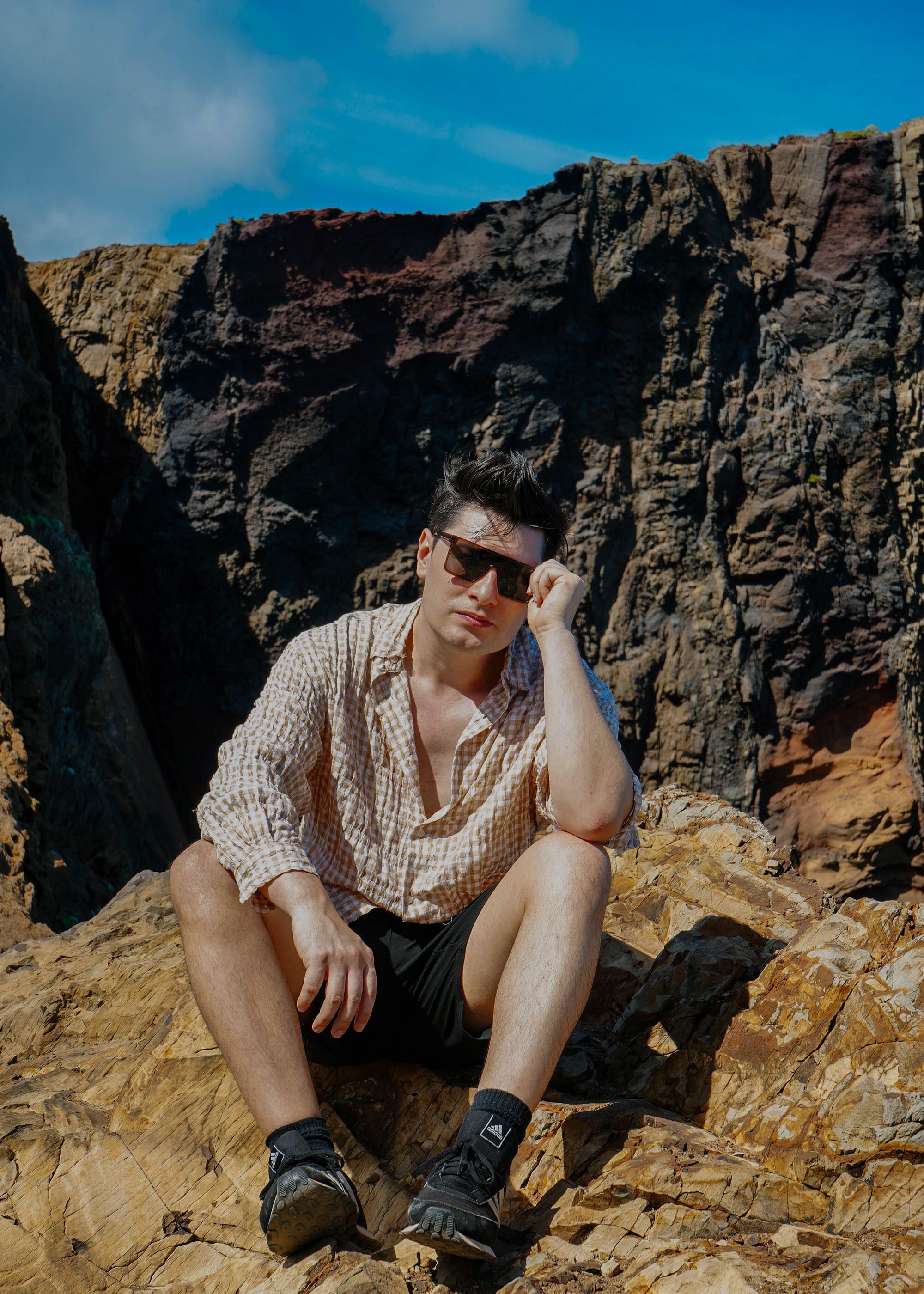 Man sitting casually on rugged rock formation under bright daylight, exuding a relaxed vibe.