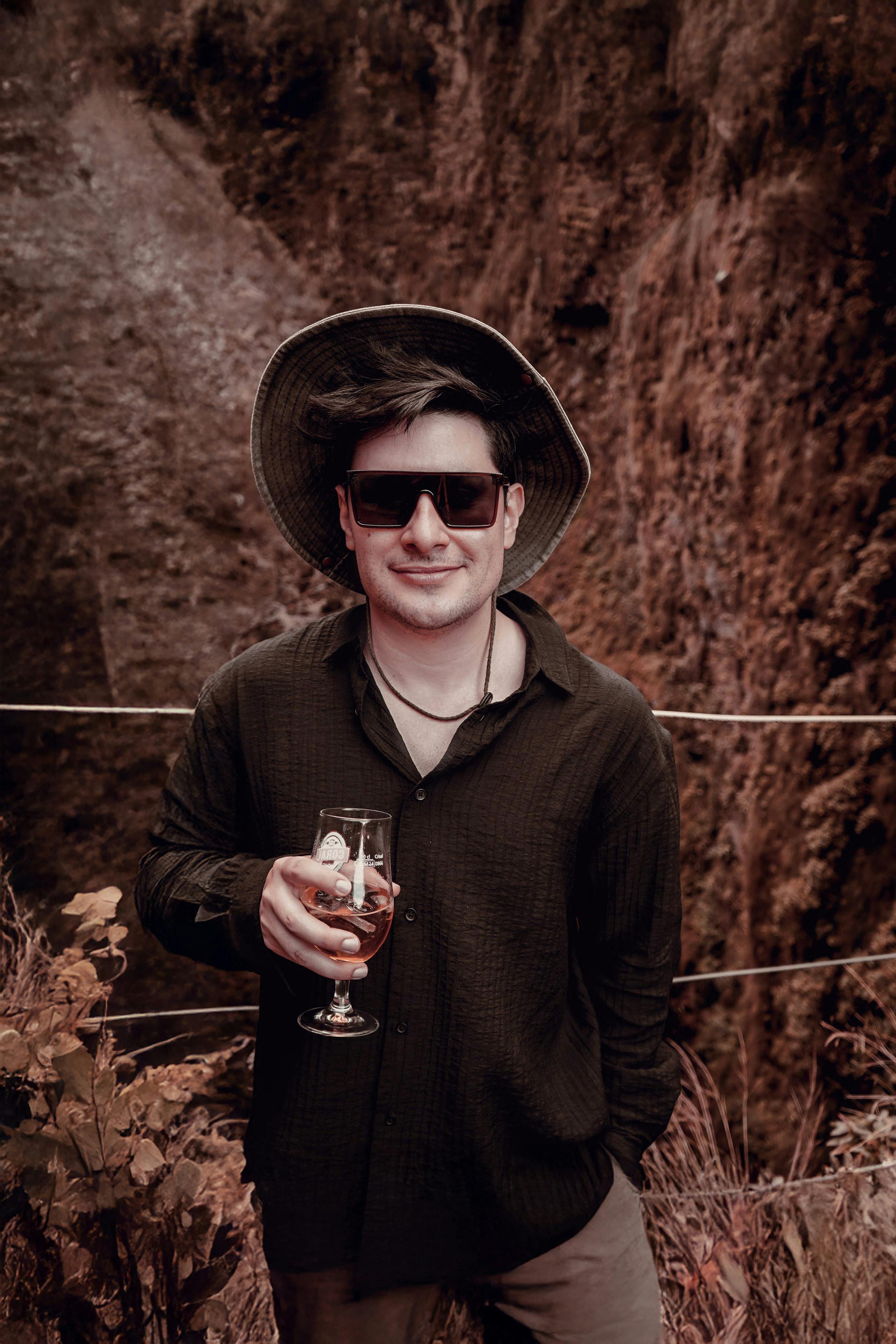 Man wearing a hat and sunglasses enjoying a drink on an outdoor adventure.