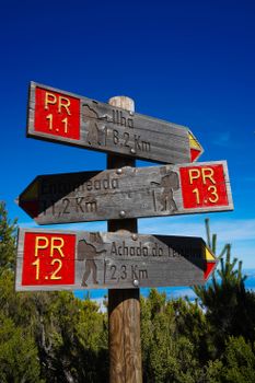 Wooden hiking trail signpost with bright red markers in a scenic outdoor setting.