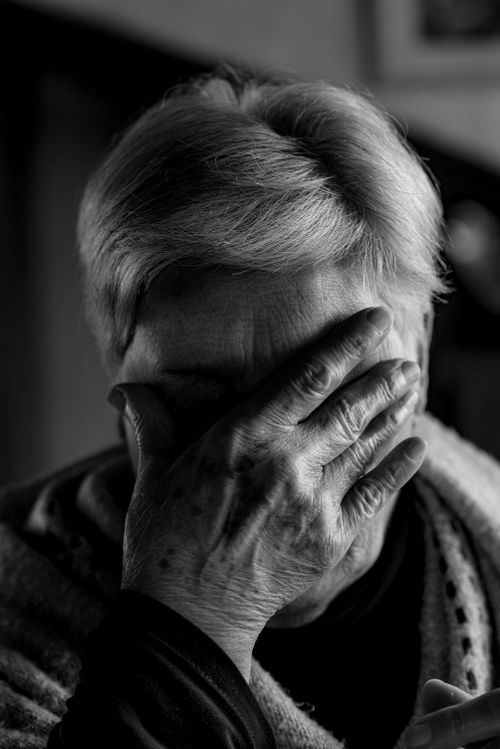 Free A senior woman covering her face in a dramatic black and white portrait. Stock Photo