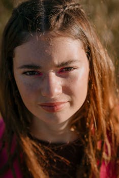 A close-up portrait of a young woman with natural makeup and sunlight outdoors.