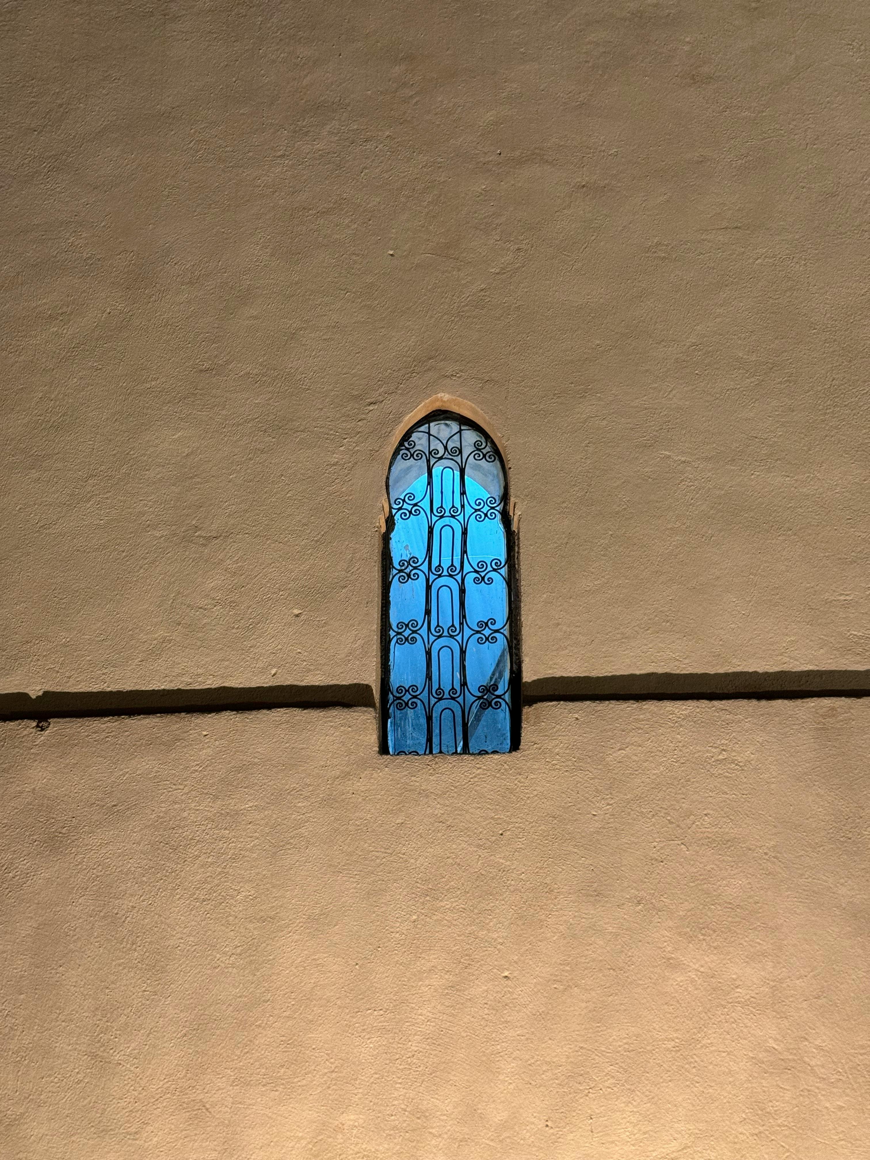 Free A historic Moroccan arched window with intricate blue patterns on a textured beige wall. Stock Photo