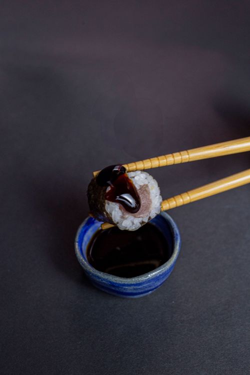 Free Top view of sushi roll held with chopsticks over a soy sauce bowl on a dark background. Stock Photo