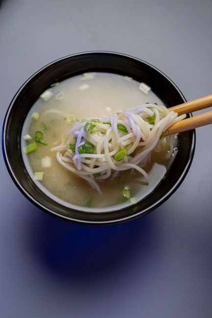 A steaming bowl of traditional Japanese noodle soup with chopsticks, garnished with green onions.