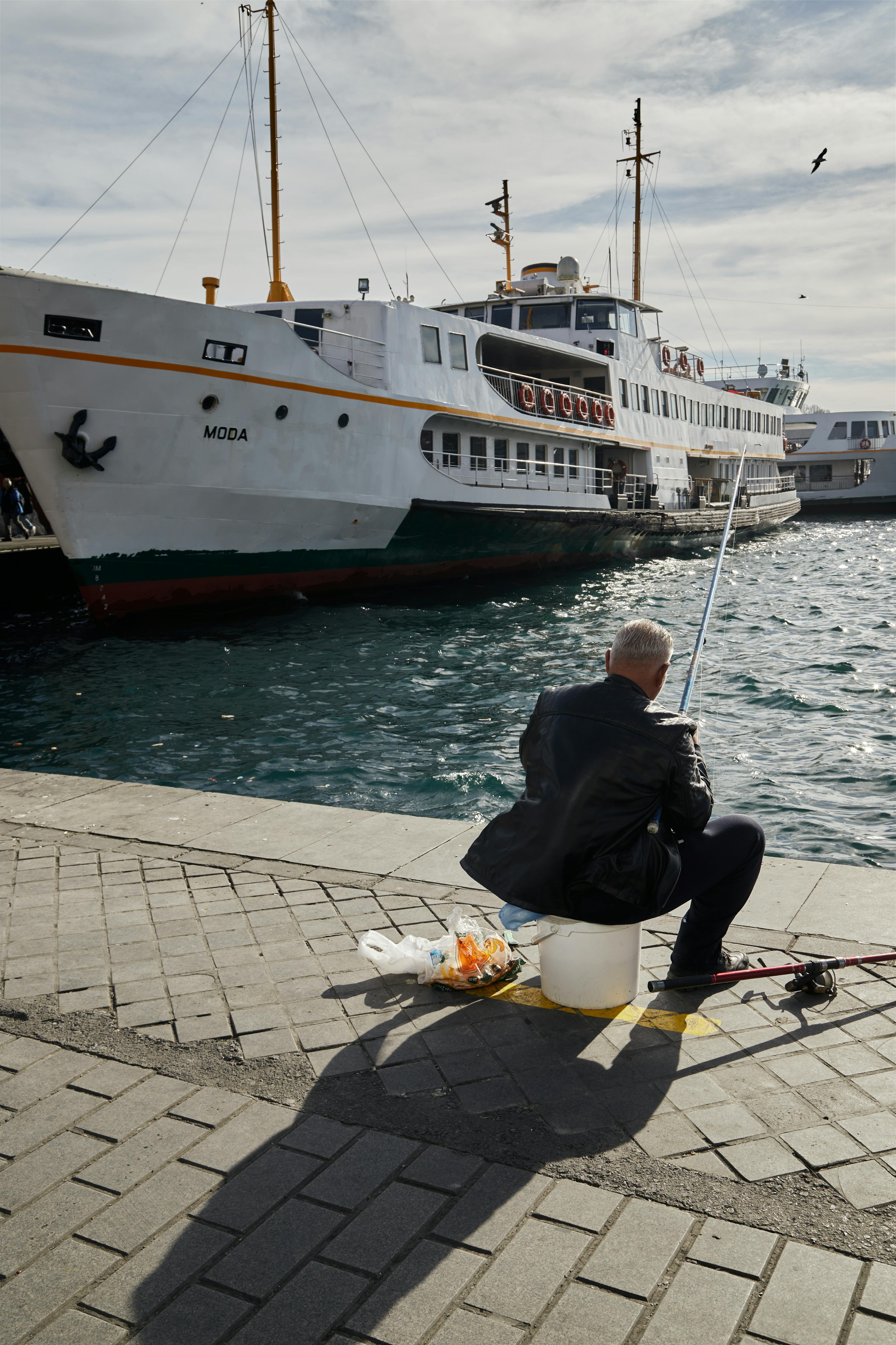 bezplatná Muž rybařící u Bosporu s trajektem jménem Moda zakotvil nedaleko v Istanbulu. Základová fotografie