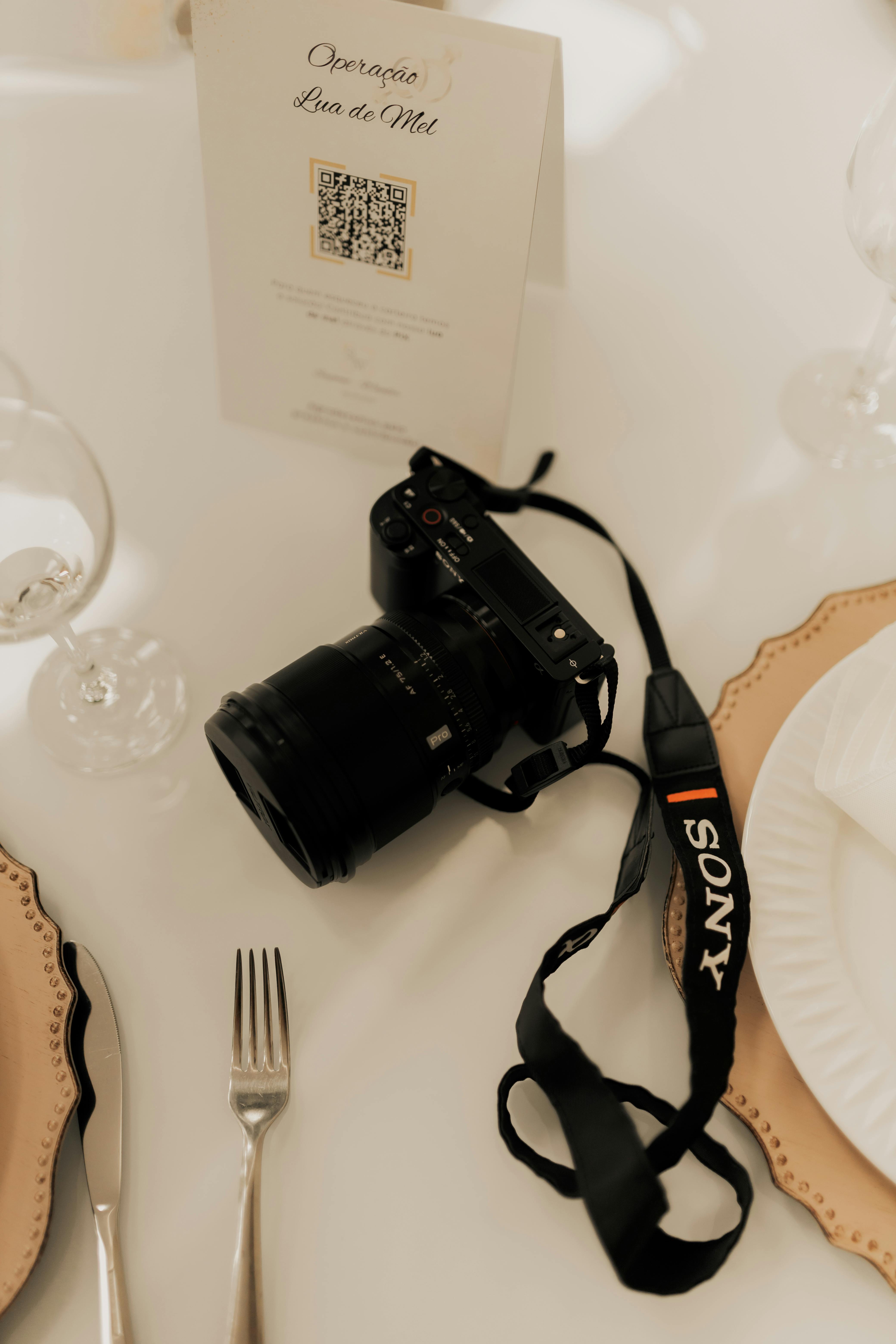 A DSLR camera on an elegant dining table, surrounded by fine dining utensils.