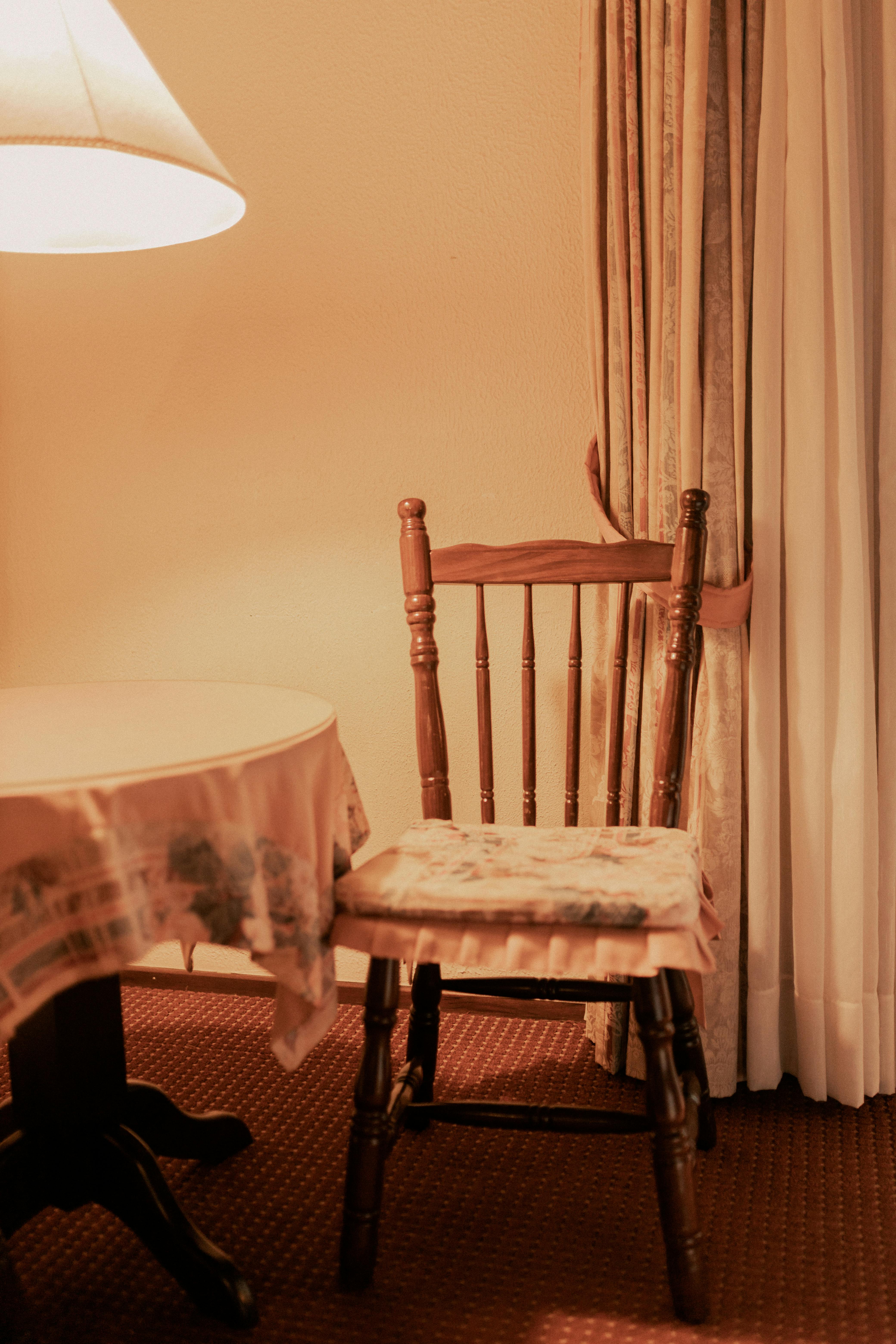 Gratuit O scenă de sufragerie caldă și primitoare, cu un scaun și o masă din lemn sub o lumină slabă. Fotografie de stoc