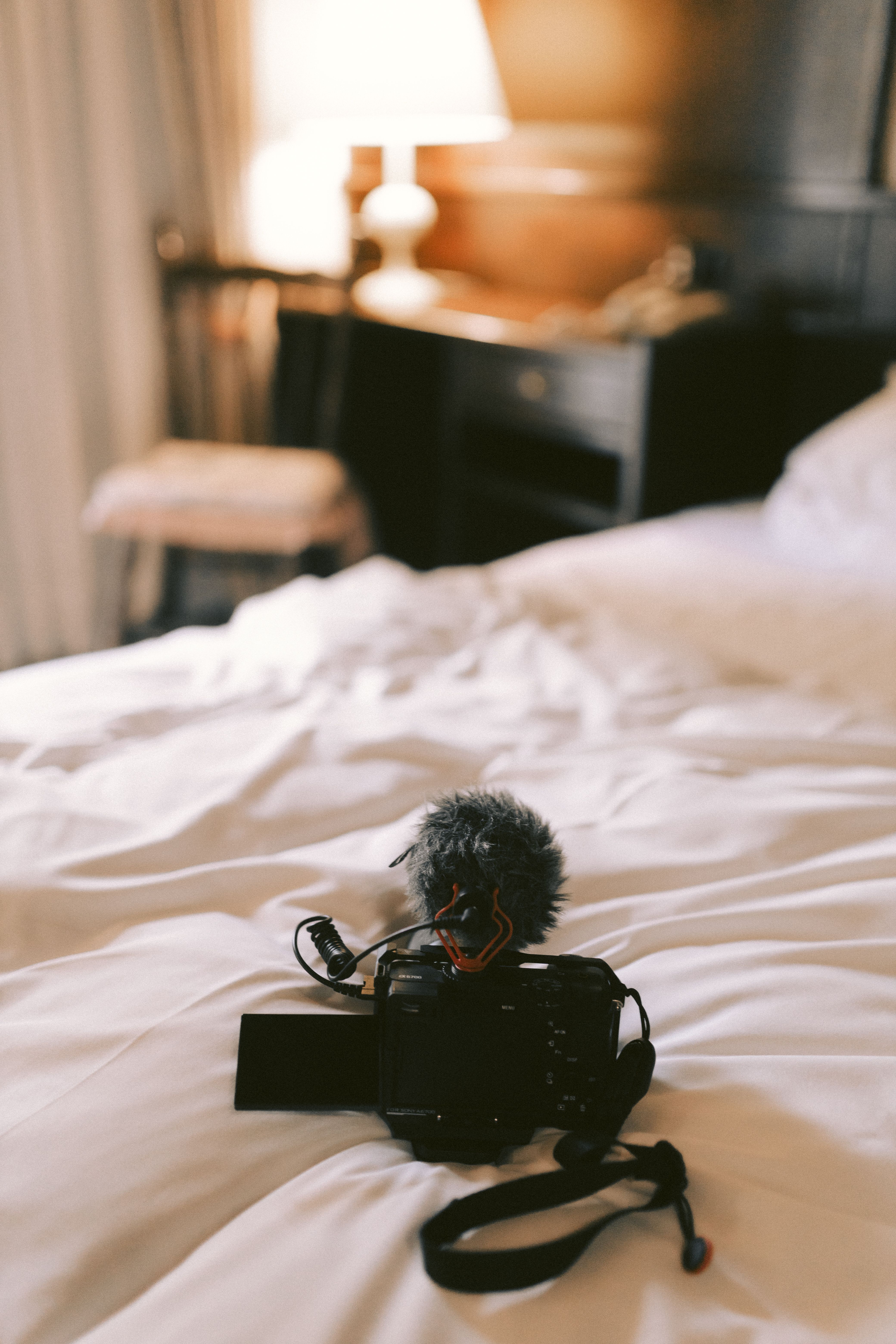 A close-up of a camera with a microphone on a bed in a warmly lit bedroom.