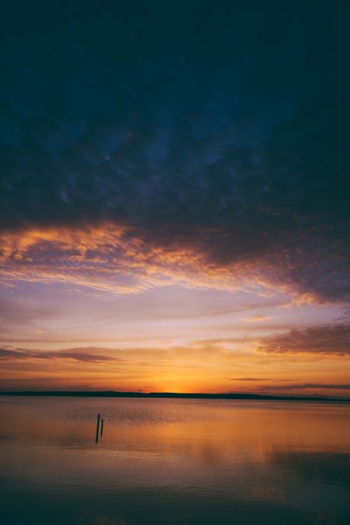 Free Captivating sunset with dramatic clouds reflecting over a calm lake, creating a peaceful atmosphere. Stock Photo