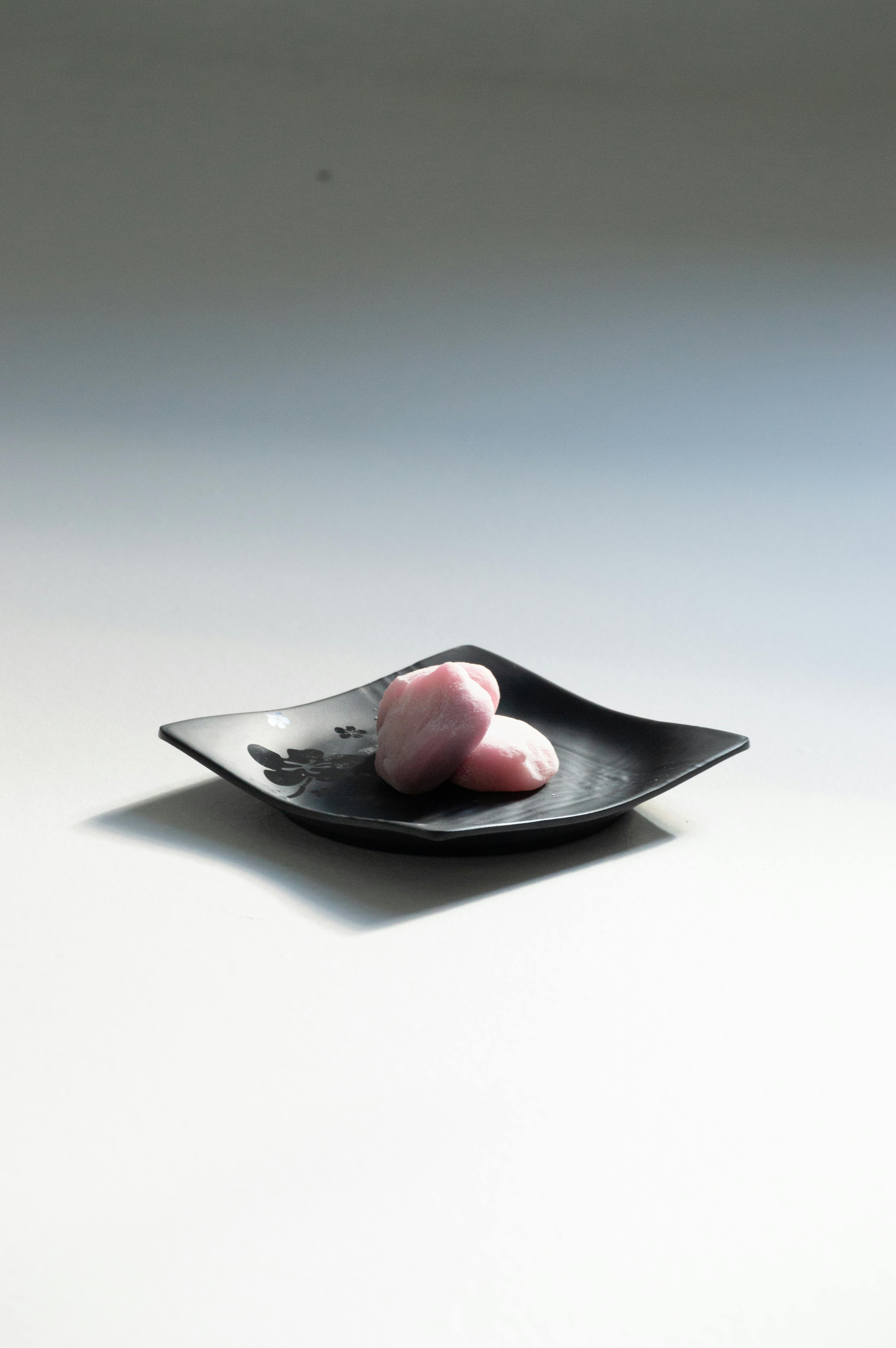 bezplatná Elegantní růžové mochi na minimalistickém černém talíři zachycené v měkkém osvětlení. Základová fotografie