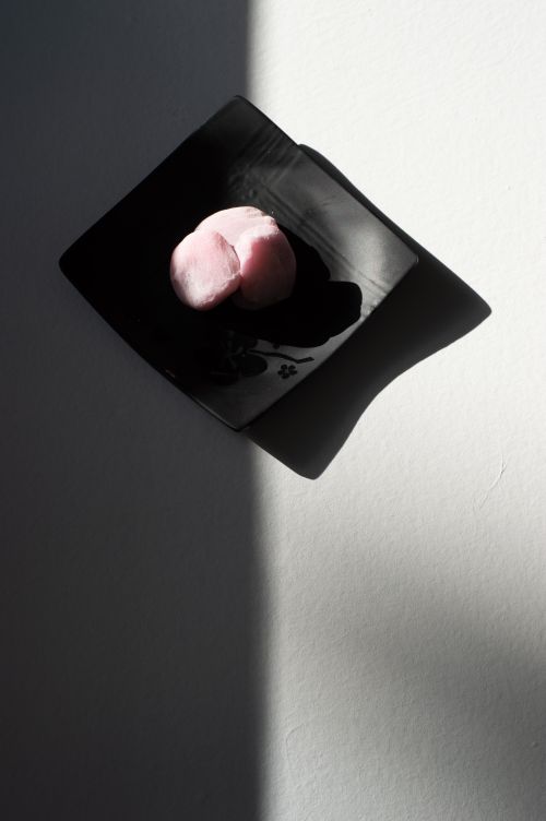 Free Artistic minimalist presentation of pink mochi on black plate, showcasing shadows and light contrast. Stock Photo