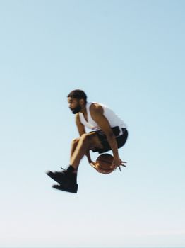 Athlete performing an impressive basketball dunk, showcasing agility and skill outdoors.