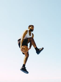 Energetic capture of basketball player performing an impressive jump against a clear sky.