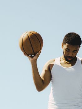Young basketball player in white tank top practicing outdoors under clear blue sky.