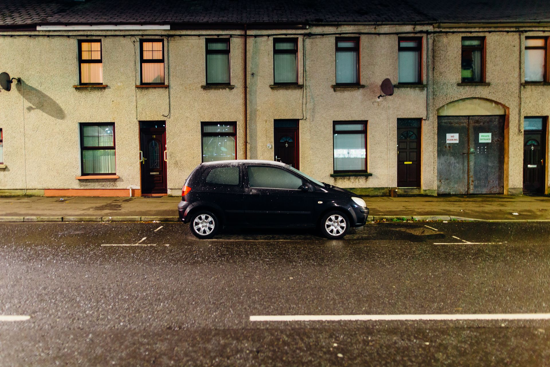 Compact car parked at night on a quiet urban street in front of residential buildings.