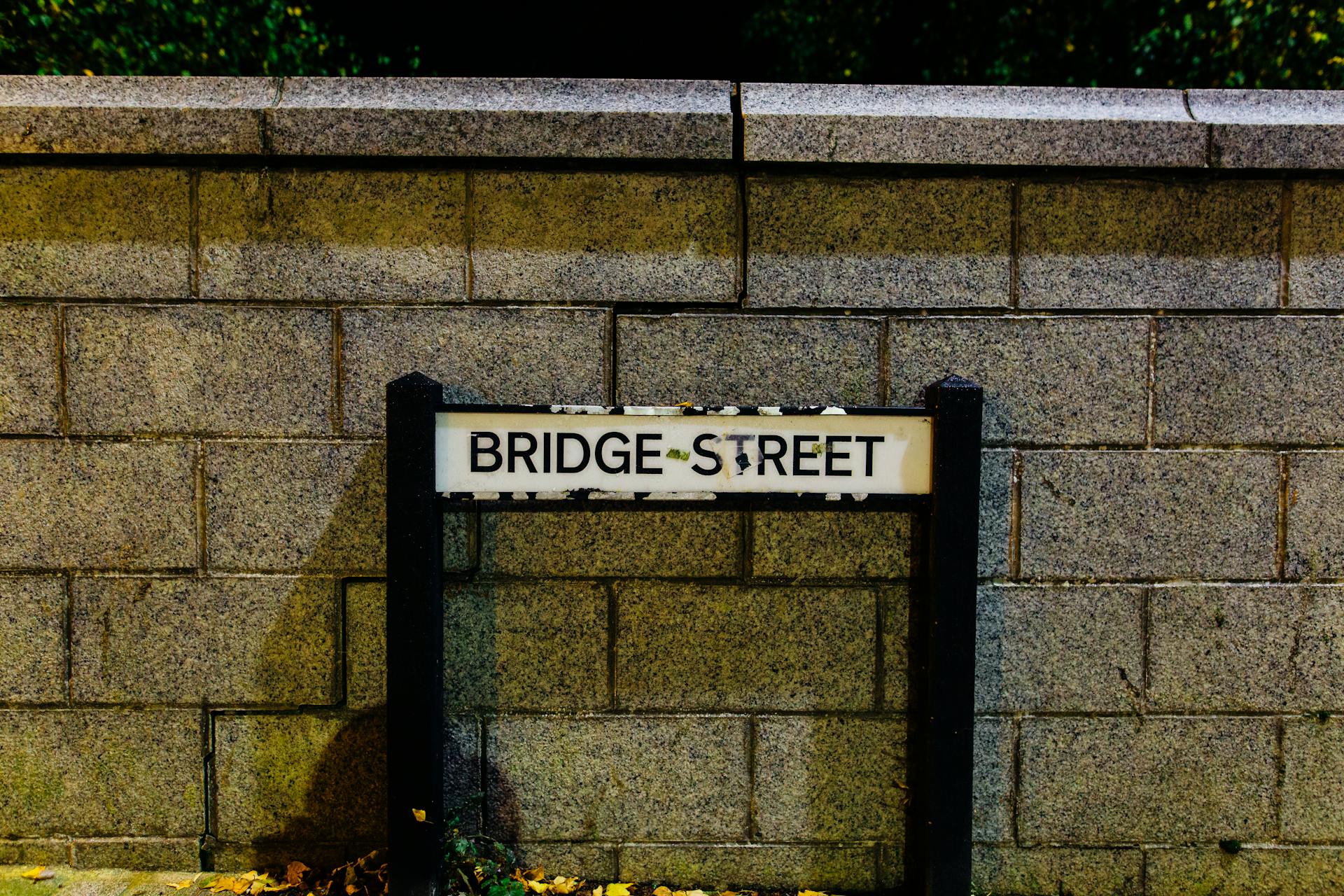 Close-up of the Bridge Street sign against a brick wall under night lighting.