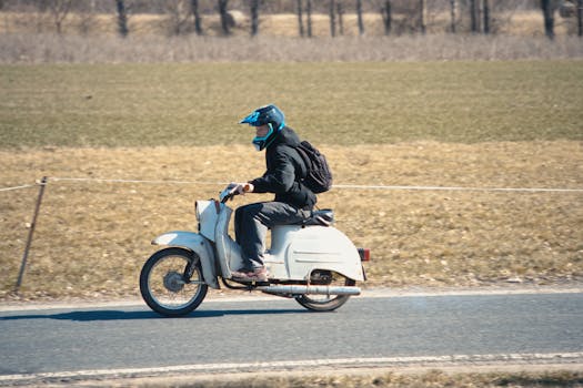 A person wearing a helmet rides a classic moped along a rural road, evoking a chill vibe.